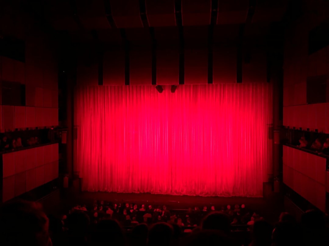 Empty theatre stage with dramatic red curtains and warm lighting